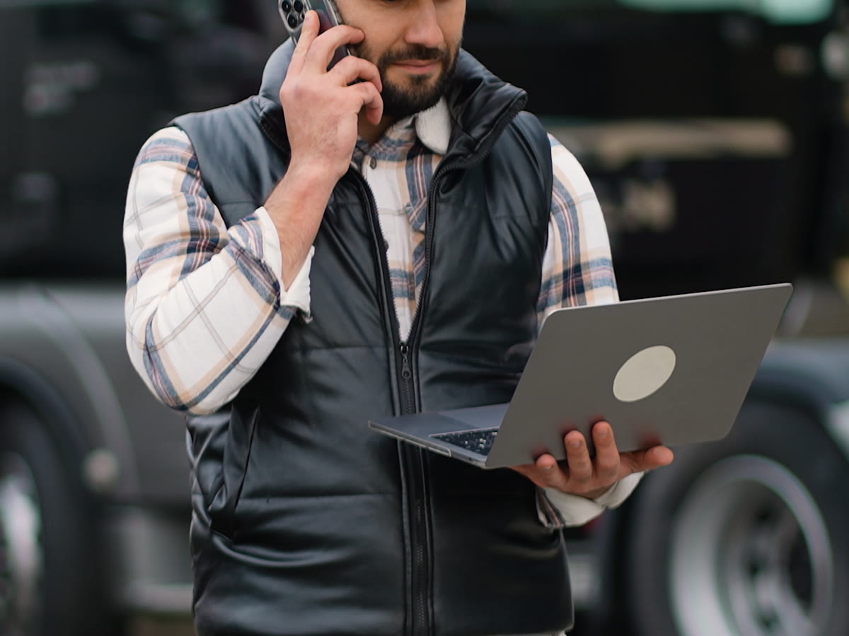 Truck driver on the phone holding a laptop beside his rig